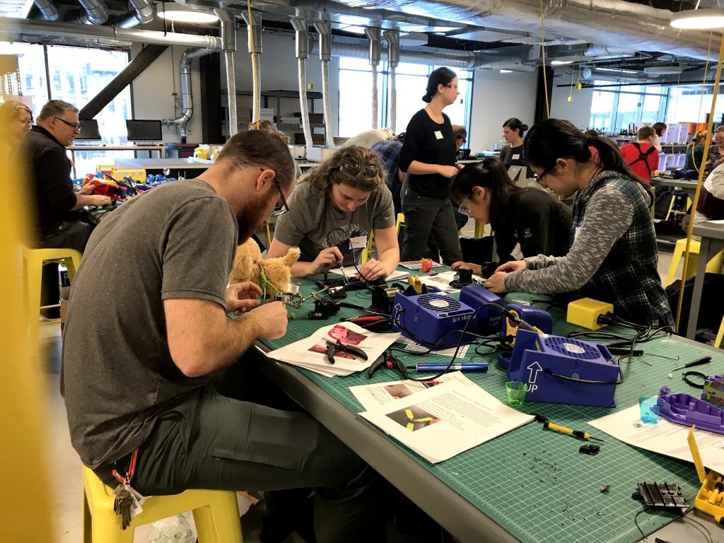 Image from a toy hackathon at a makerspace where people are gathered to modify toys to make them switch accessible.